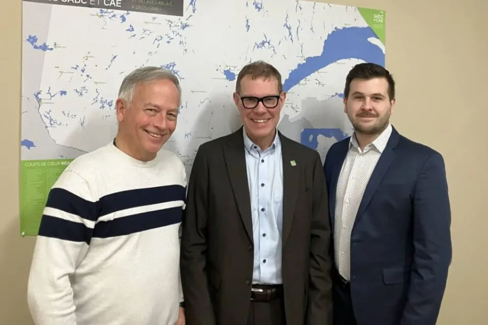 Trois hommes souriants devant une carte murale