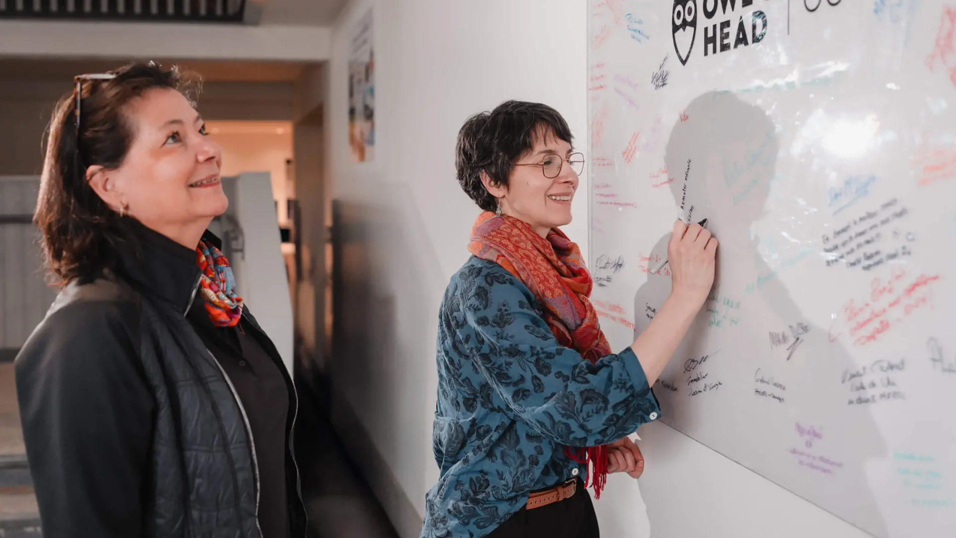Two women signing office whiteboard wall