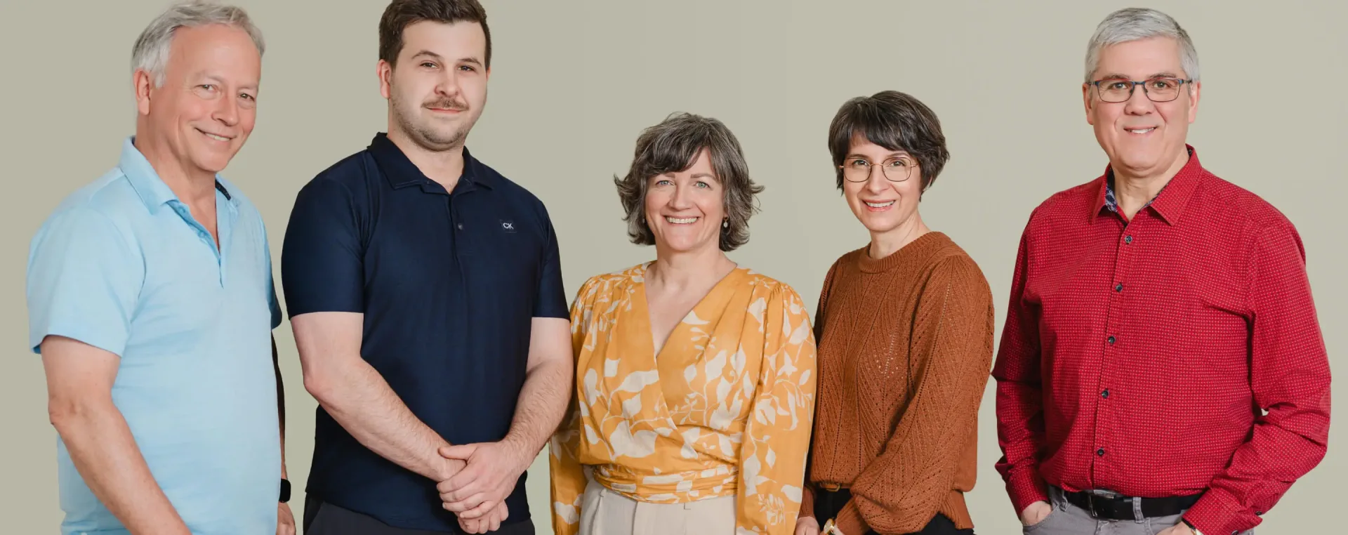 Cinq adultes souriants posant sur fond neutre